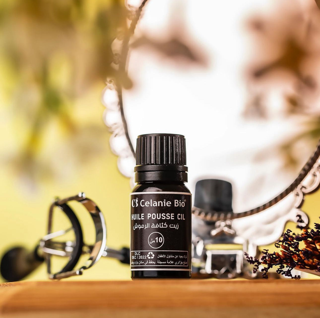 Flacon d’huile naturelle pour cils avec applicateur, posé sur une surface élégante, accompagné de graines de ricin et d’huiles végétales en arrière-plan.